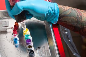 Close-up of Tattoo artist holding tattoo gun with needle in yellow ink well