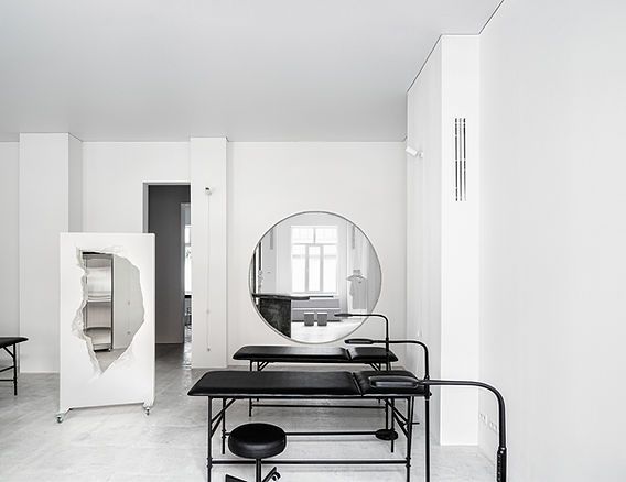 Minimalist white studio with black treatment tables and circular mirror